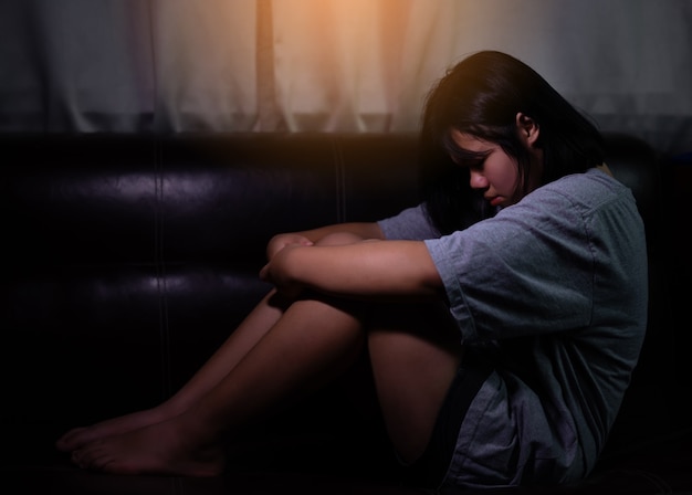 Foto menina adolescente com depressão ou triste sentada sozinha no quarto escuro. transtorno depressivo maior. conceito solitário e problemas de saúde.