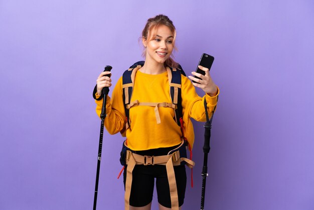 Menina adolescente com mochila e bastões de trekking na parede roxa isolada fazendo uma selfie