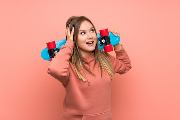 Menina adolescente com skate sobre fundo rosa isolado