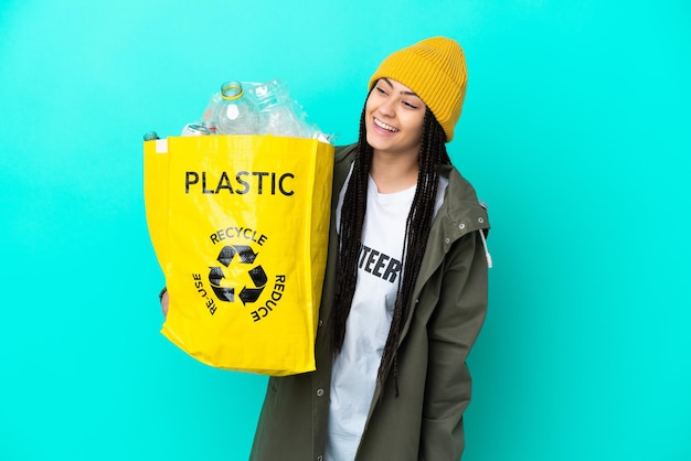 Foto menina adolescente com tranças segurando um saco para reciclar olhando para o lado e sorrindo