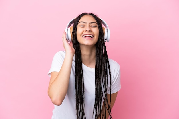 Menina adolescente com tranças sobre fundo rosa isolado ouvindo música