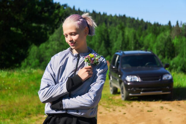 Menina adolescente com um buquê de flores silvestres na natureza no fundo do carro