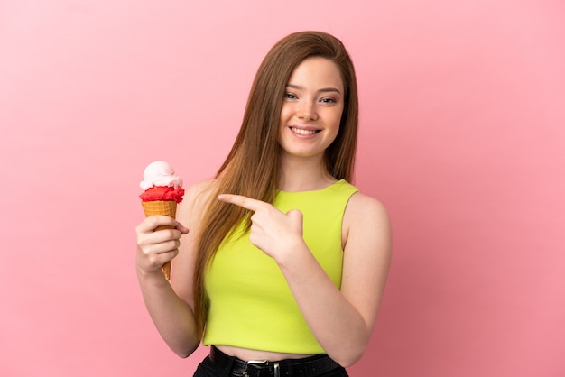 Menina adolescente com um sorvete de corneta sobre fundo rosa isolado apontando para o lado para apresentar um produto