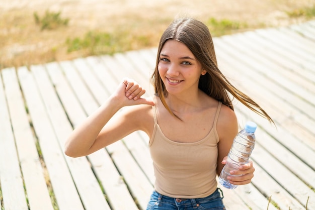 Menina adolescente com uma garrafa de água ao ar livre orgulhosa e satisfeita