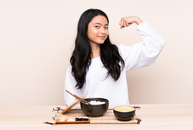 Menina adolescente comendo comida asiática isolada em bege, fazendo um gesto forte