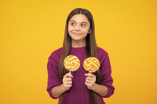 Menina adolescente comendo pirulito de açúcar Doces e doces para crianças Criança come picolé de pirulito sobre fundo amarelo isolado Loja de doces de caramelo gostoso