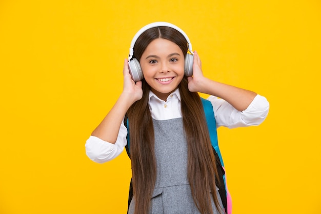 Menina adolescente da escola em fones de ouvido com mochila escolar Fundo isolado de estudante adolescente Aprendendo música Garota feliz enfrenta emoções positivas e sorridentes