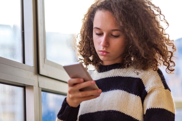 Menina adolescente de cabelo encaracolado usando telefone celular