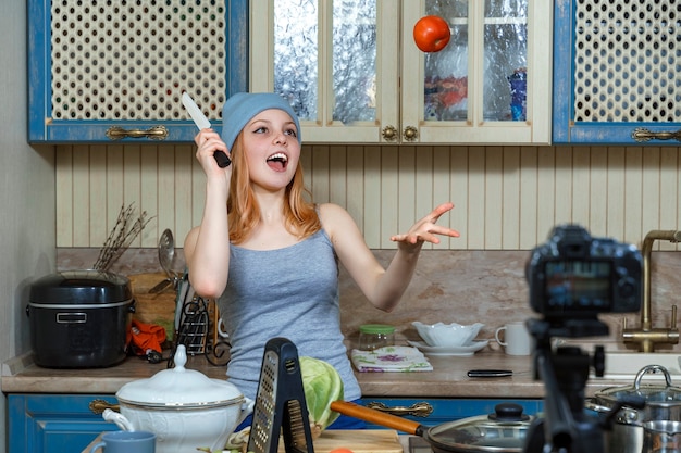 Menina adolescente de chapéu azul e camiseta escreve vídeo para blog de comida e faz truques com tomates.