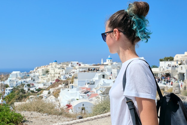 Menina adolescente descansando na ilha grega de santorini, mulher olhando para longe, arquitetura de fundo branco da vila de oia, mar, céu nas nuvens, espaço de cópia