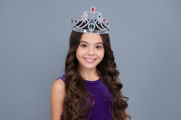 Menina adolescente egoísta celebra a vitória do sucesso Criança adolescente na coroa da rainha isolada em fundo cinza Princesa na tiara Festa de formatura Menina feliz enfrenta emoções positivas e sorridentes