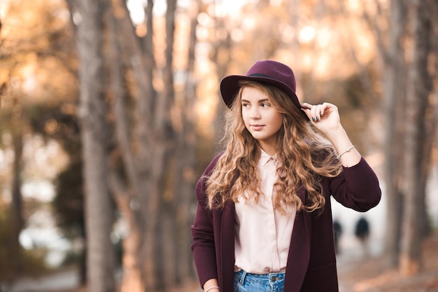 Menina adolescente elegante vestindo jaqueta da moda e chapéu, posando no parque