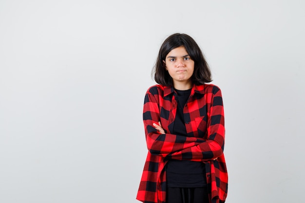 Menina adolescente em camisa casual, segurando os braços cruzados e olhando mal-humorada, vista frontal.