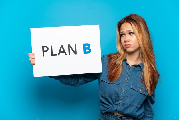 Menina adolescente em um fundo azul isolado segurando um cartaz com a mensagem plano b com expressão triste