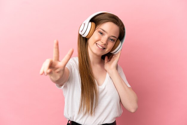 Menina adolescente em um fundo rosa isolado ouvindo música e cantando