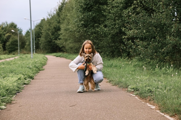 Menina adolescente em um passeio no parque de verão com seu animal de estimação Yorkshire terrier. Criança passeando com um cachorro