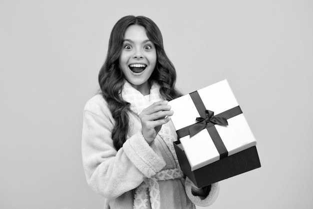 Menina adolescente espantada Criança adolescente segurando caixa de presente em fundo amarelo isolado Presente para aniversário de crianças Caixa de presente de Natal ou Ano Novo Expressão animada alegre e feliz