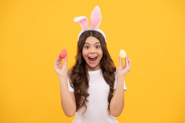 Menina adolescente espantada em orelhas de coelho segura ovos na páscoa de fundo amarelo