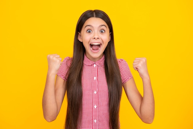 Menina adolescente espantada Expressão animada alegre e feliz Criança adolescente fazendo gesto de vencedor comemora apertando dizer sim isolado no retrato de estúdio de fundo amarelo