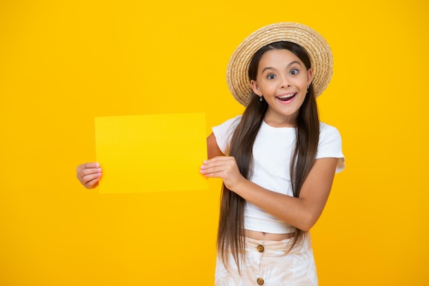 Menina adolescente espantada segura papel de anúncio vazio com espaço de cópia em fundo amarelo