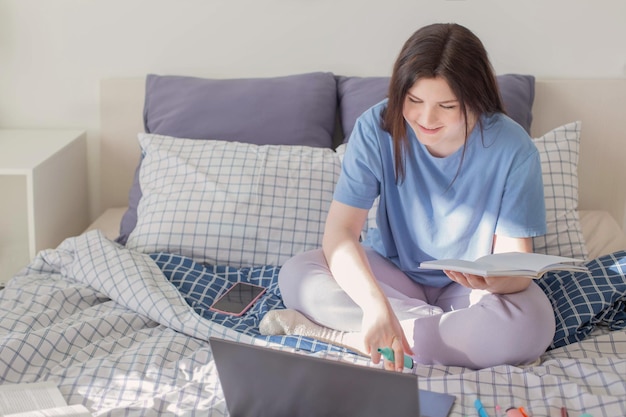 Menina adolescente estudando em casa na cama com laptop