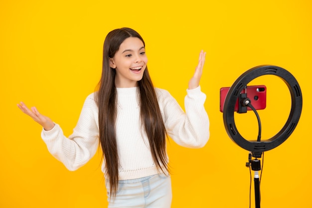 Menina adolescente falando na frente da câmera para vlog isolado em fundo amarelo Adolescente trabalhando como blogueiro gravando vídeo blog