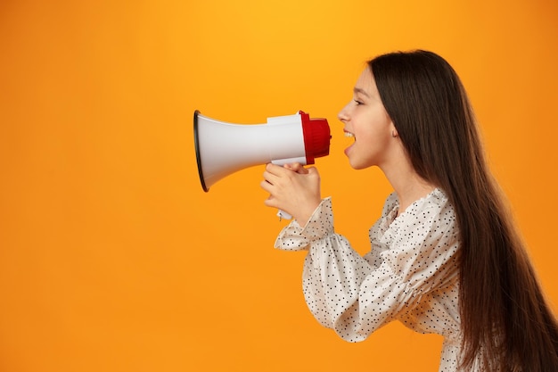 Menina adolescente fazendo anúncio com megafone em fundo amarelo