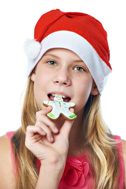 Foto menina adolescente feliz com boné vermelho comendo biscoito de natal isolado