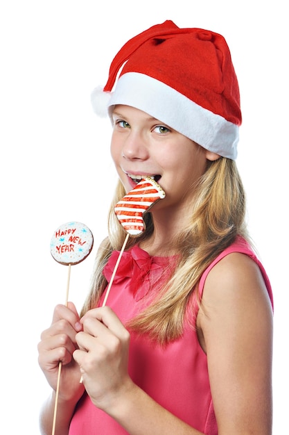Menina adolescente feliz com boné vermelho comendo biscoito de Natal isolado