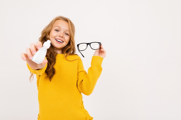 Menina adolescente feliz com cabelo vermelho, calças com capuz e amarelas mantém lentes de contato e óculos isolados no branco