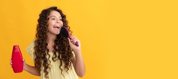 Menina adolescente feliz com cabelos longos e encaracolados segura a garrafa de xampu cantando na escova de cabelo divertida Banner do cabeçalho do pôster do estúdio de cuidados com os cabelos da menina infantil com espaço de cópia