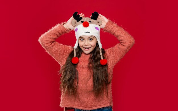 menina adolescente feliz com chapéu de moda de inverno isolado em vermelho menina adolescente usa suéter e chapéu de moda de inverno em estúdio moda de inverno para menina adolescente modelo de moda de menina adolescente com chapéu de orelha de inverno