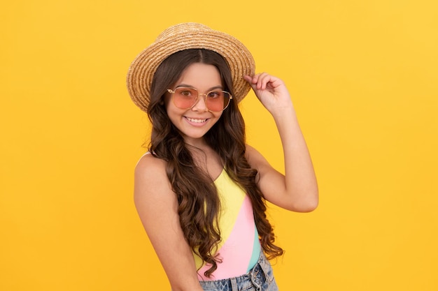 Menina adolescente feliz com chapéu de palha de verão e óculos tem cabelo encaracolado na felicidade de fundo amarelo