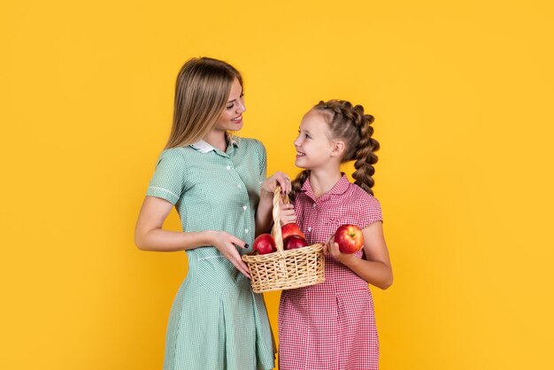 Menina adolescente feliz e sua mãe com maçãs na cesta cheia de vitamina colhida da colheita do outono