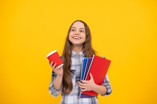 Menina adolescente feliz em camisa quadriculada segurando xícara de café e notebook em fundo amarelo, educação