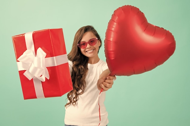 Menina adolescente feliz em óculos de sol dando caixa de presente e dia dos namorados balão de coração de festa dia dos namorados