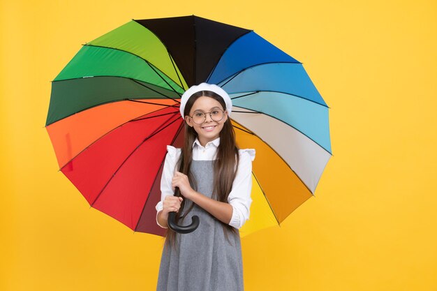 Menina adolescente feliz em óculos e boina sob guarda-chuva colorido para proteção contra chuva na temporada de outono, otimista.