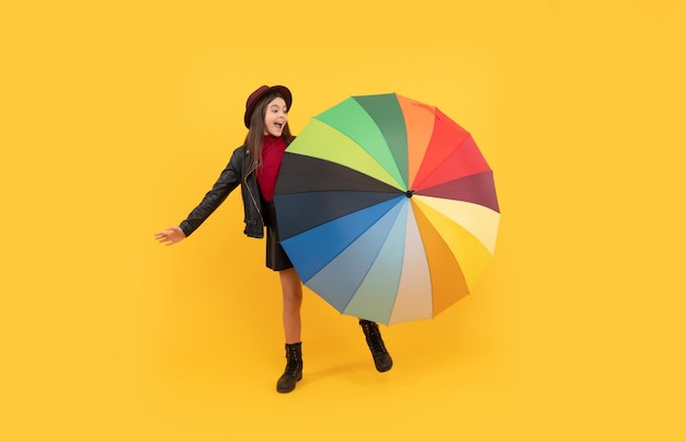 Menina adolescente feliz em roupas de chapéu e couro se divertindo com o humor do outono do guarda-chuva arco-íris