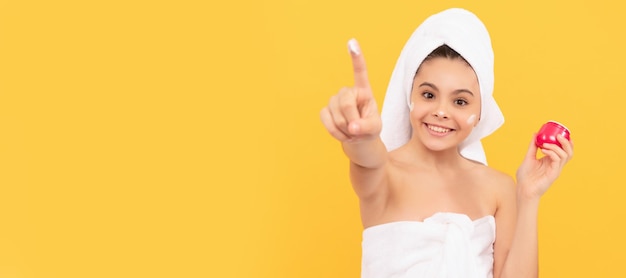 Menina adolescente feliz em toalha de banho aplique foco seletivo de creme facial Cosméticos e cuidados com a pele para design de cartaz de criança adolescente Banner de menina de beleza com espaço de cópia