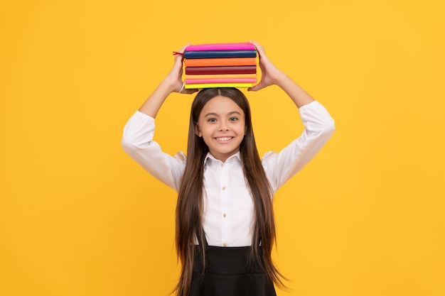 Menina adolescente feliz em uniforme escolar detém conhecimento de pilha de livros