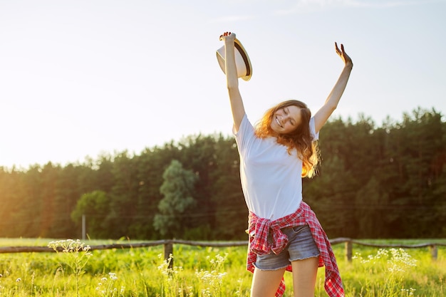 Menina adolescente feliz pulando com o chapéu. Alegria de férias verão natureza pôr do sol, fundo de bela paisagem cênica, espaço de cópia