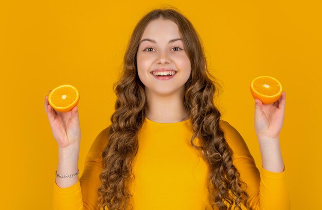 menina adolescente feliz segurando frutas laranja em fundo amarelo