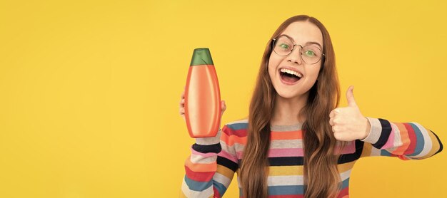 Menina adolescente feliz usa garrafa de xampu criança com condicionador de cabelo Banner de cabeçalho de cartaz de estúdio de cuidados com o cabelo de menina infantil com espaço de cópia