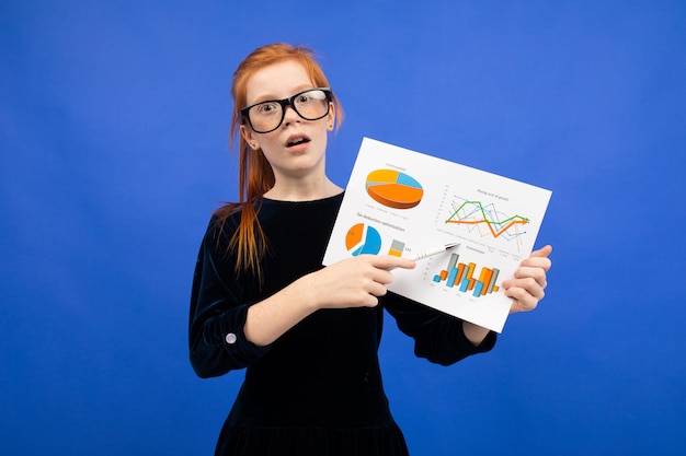 Menina adolescente inteligente de óculos e um vestido preto mostra estatísticas com gráficos de pizza e gráficos azuis