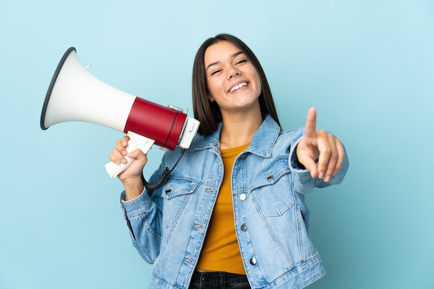 Menina adolescente isolada em amarelo segurando um megafone e sorrindo enquanto aponta para a frente