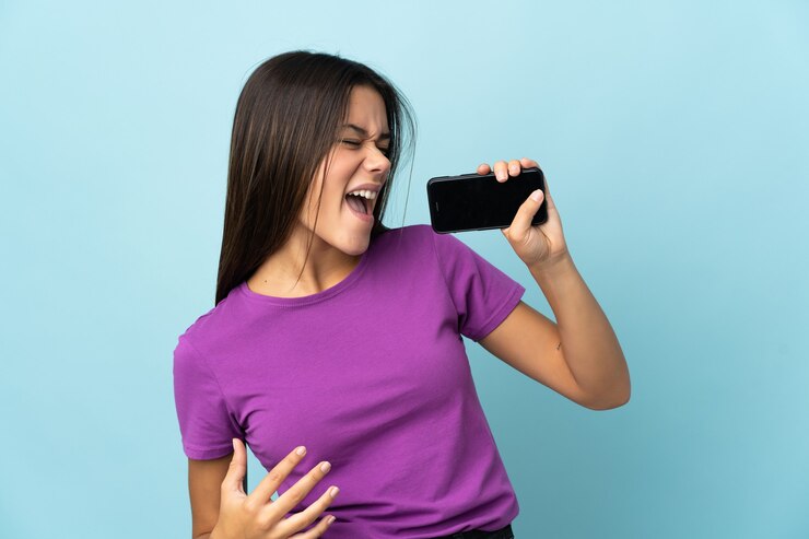 Foto menina adolescente isolada em rosa usando telefone celular e cantando