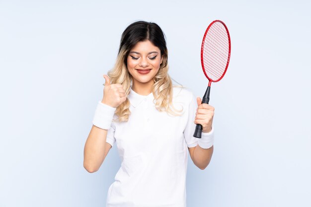 Menina adolescente jogando badminton isolado na parede azul, dando um polegar para cima gesto