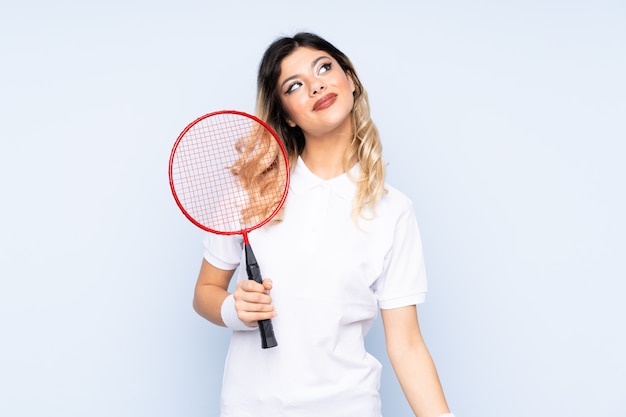 Menina adolescente jogando badminton na parede azul, rindo e olhando para cima