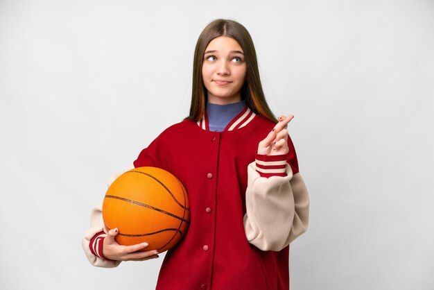 Menina adolescente jogando basquete sobre fundo branco isolado com os dedos cruzando e desejando o melhor