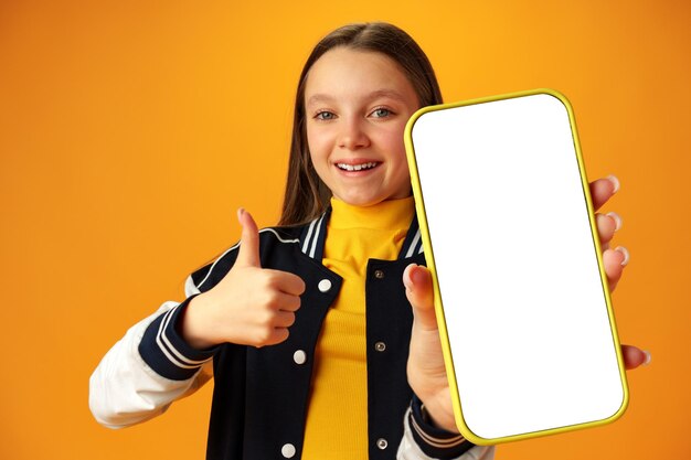 Menina adolescente mostrando a tela do smartphone com espaço de cópia sobre fundo amarelo